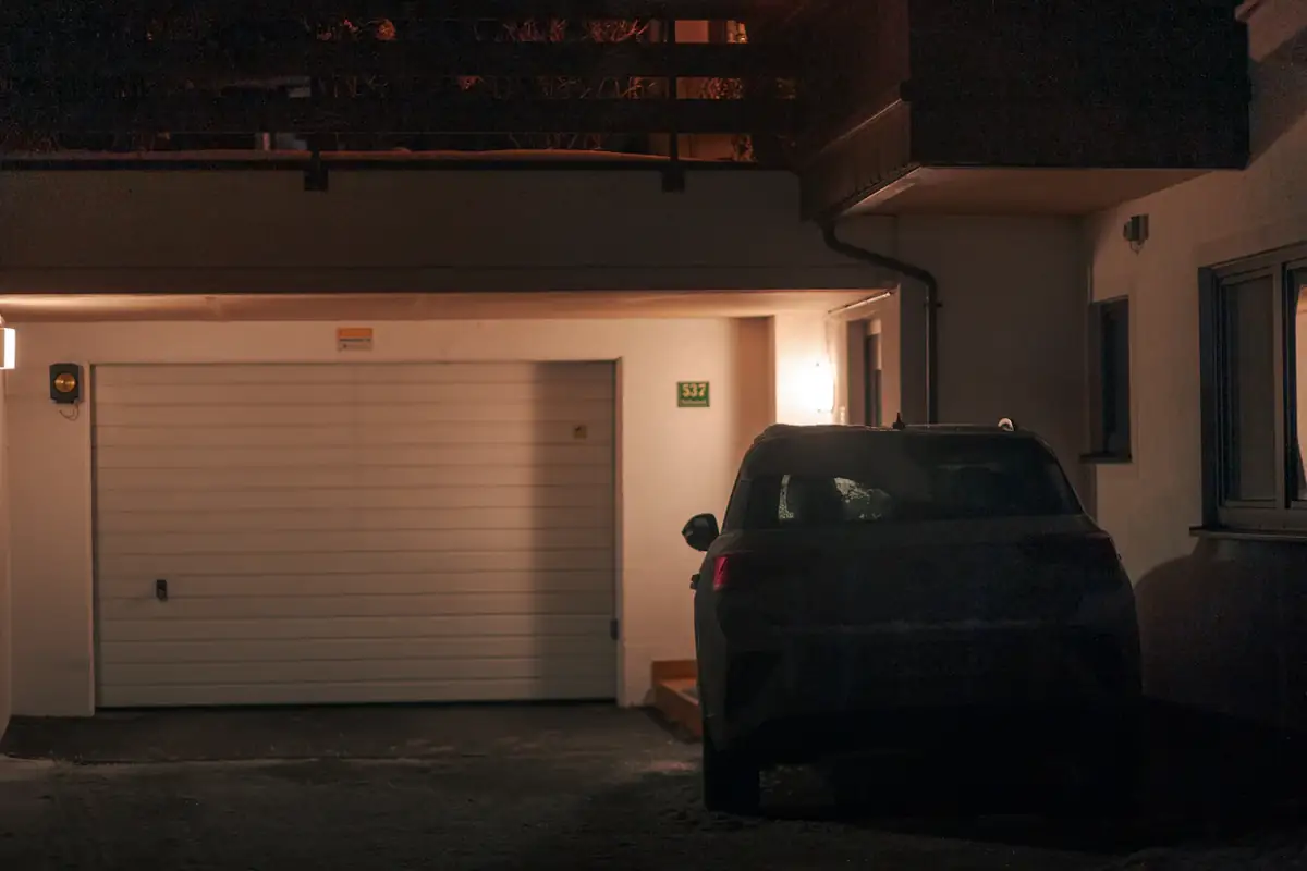 A car parked in front of a lit garage at night