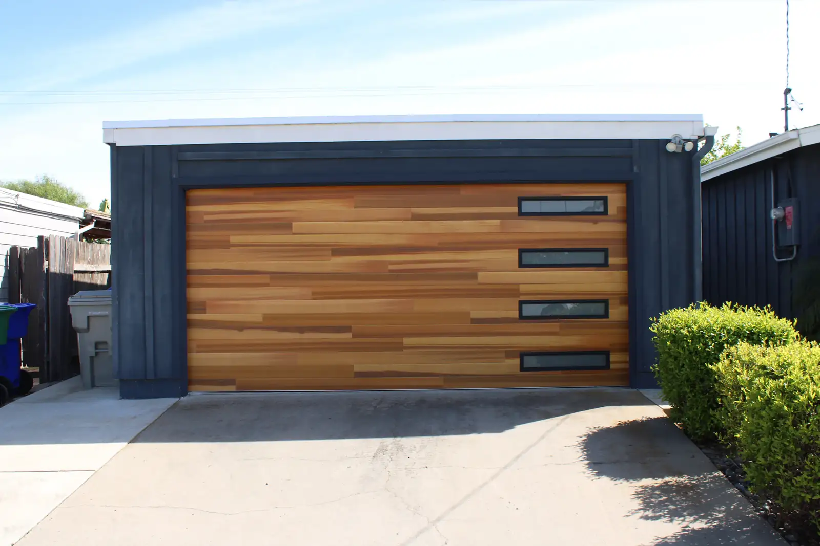 A modern wood-panel garage door with a row of windows on a dark house